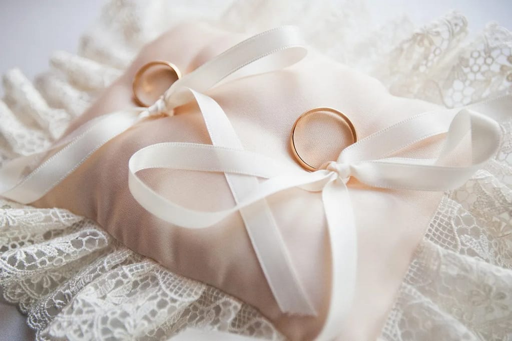 Two gold geometric rings displayed on a satin pillow with white ribbons and lace, showcasing elegant styling ideas for minimalist geometric rings.